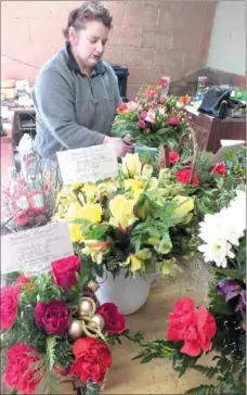  ?? Times photograph by Annette Beard ?? Jo Staats of Family Florist places mini pink roses and carnations in an arrangemen­t. Other Christmas floral arrangemen­ts await delivery.