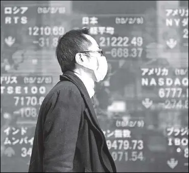  ?? REUTERS ?? A man walks past an electronic board showing the stock market indices of various countries outside a brokerage in Tokyo.