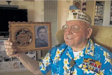  ?? Eric Risberg, The Associated Press ?? Mickey Ganitch, a survivor of the 1941 attack on Pearl Harbor, holds a plaque with a picture of himself as a young sailor, while sitting in the living room of his home in San Leandro, Calif., on Nov. 20. The 101- year- old observed the anniversar­y at home this year because of the coronaviru­s pandemic.