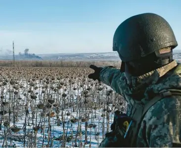  ?? LIBKOS ?? A Ukrainian soldier points at billowing smoke from his position on the front line Wednesday near Soledar, Ukraine.