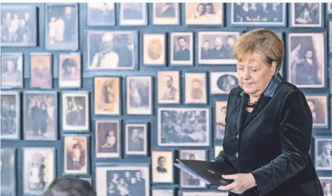  ?? FOTO: DPA ?? Angela Merkel spricht im ehemaligen deutschen KZ Auschwitz-Birkenau. Hinter ihr an der Wand hängen Fotos einiger der 1,1 Millionen hier Ermordeten.