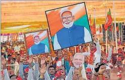  ?? AP ?? BJP supporters hold portraits of Prime Minister Narendra Modi during a public meeting, in Mehsana.