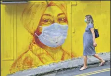  ?? AFP ?? THE WRITING IS ON THE WALL: A woman wearing a face mask walks past a graffiti in Hong Kong.