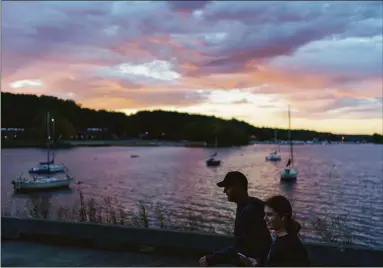  ?? David Goldman / Associated Press ?? A couple walks along the St. Croix River as the sun rises in Hudson, Wis., on Sept. 30. Hudson, a onetime ragged-at-the-edges riverside town, has become a place of carefully tended 19th-century homes, tourists wandering main street boutiques and emigres from Minneapoli­s and St. Paul looking for cheaper real estate and a quieter place to raise their kids.