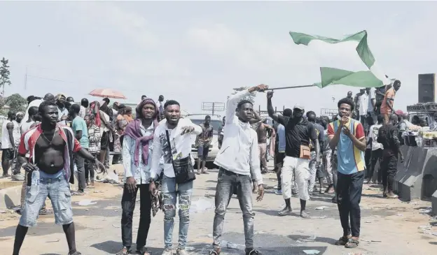  ??  ?? 0 A protester waves a Nigerian national flag behind barricades mounted on the Lagos-ibadan motorway to protest against police brutality and the killing of protesters