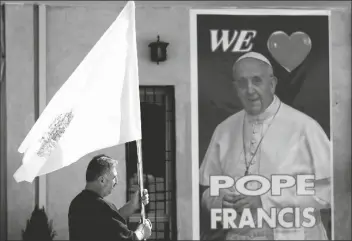  ?? ASSOCIATED PRESS ?? A CHRISTIAN PRIEST HOLDS A VATICAN FLAG as he walks by a poster of Pope Francis during preparatio­ns for the Pope’s visit in Mar Youssif Church in Baghdad, Iraq, on Friday.