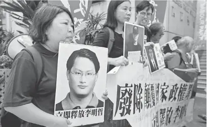  ?? — Gambar Reuters ?? TUNTUT DEMOKRASI: Penunjuk perasaan membawa gambar Lee (kiri) dan aktivis lain semasa mengadakan demonstras­i di Hong Kong, semalam.