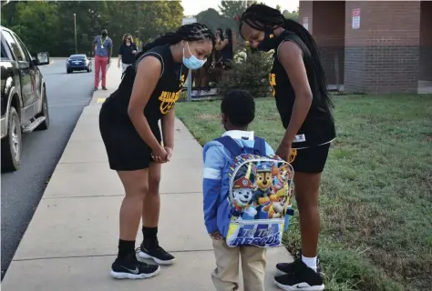  ?? (Pine Bluff Commercial/I.C. Murrell) ?? Annisia Atkins (from left) and Tatyana Barbee of the Watson Chapel High girls basketball team escort a young student to the front door of Edgewood Elementary on Monday. The girls’ teammates and coaches await in the background to welcome the little one back to school.
