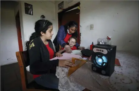  ?? FERNANDO VERGARA — THE ASSOCIATED PRESS ?? Fanny Mendez, mother of Marlene Beltran, 14, and Felipe Beltrán, 5, helps her children at home to make a cube out of paper as they listen to an hourlong lesson broadcast by the Bacata Stereo radio station in Funza, Colombia, on Wednesday.