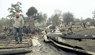  ?? BEN MARGOT/THE ASSOCIATED PRESS ?? A man inspects a neighbour’s home in the Coffey Park area of Santa Rosa, Calif., on Tuesday. An onslaught of wildfires across a wide swath of Northern California is tearing through both tiny rural towns and urban subdivisio­ns.