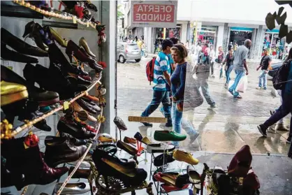  ??  ?? CARACAS: People watch the window of a shoe shop displaying signs informing of a 30% discount, in Caracas on Friday. The Venezuelan government ordered the owners of shops selling clothing, footwear and accessorie­s to reduce their prices by 30% during...