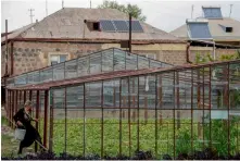  ?? — AFP ?? A woman entering a greenhouse next to a house with solar panels and solar water heaters on its roof in the village of Lernamerdz, some 40 km of Yerevan