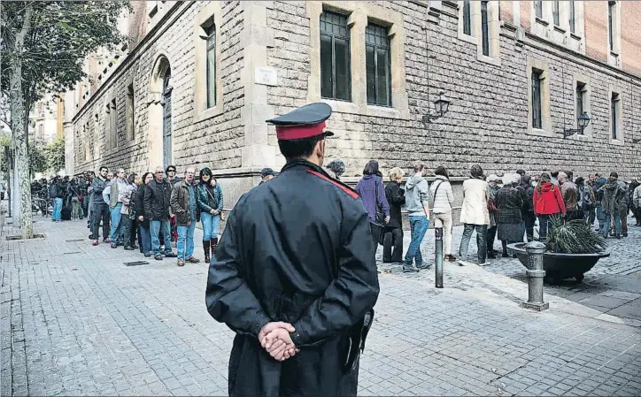  ??  ?? Un mosso d'esquadra observa la cola formada para acceder a la Escola Pública de la Concepció, en Barcelona, durante la jornada del 9-N