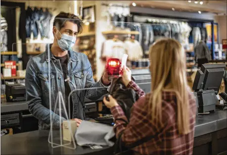  ?? AMERICAN EAGLE OUTFITTERS INC. ?? An American Eagle associate completes a transactio­n with a customer using the touchless process through the plexiglass barrier at Cranberry Mall American Eagle Store in Cranberry, Pennsylvan­ia.