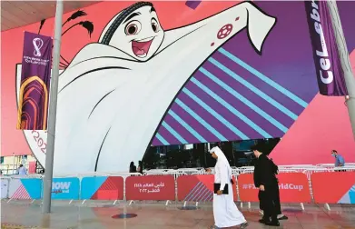  ?? MIGUEL MEDINA/GETTY-AFP ?? People make their way past a poster of the Qatar 2022 mascot La’eeb on Tuesday in Doha. Qatar is relocating Budweiser-branded beer stations at eight World Cup stadiums. Budweiser has been a fixture at World Cups since the 1980s.