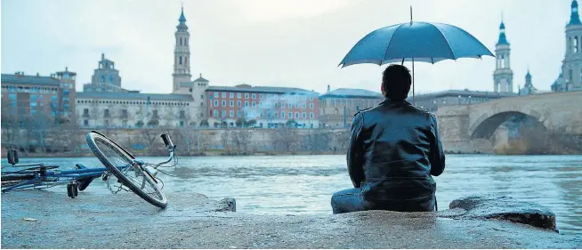  ?? MARCOS CEBRIÁN ?? Pepe Lorente, caracteriz­ado como Mauricio Aznar, sentado junto al Ebro con su bici al lado. Al fondo, el puente de Piedra y la basílica del Pilar.