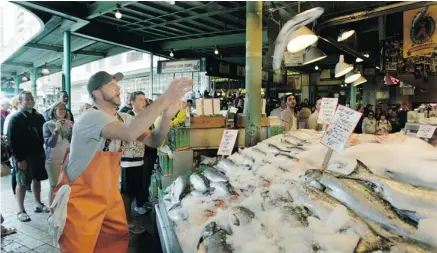  ?? PHOTOS: TED S. WARREN/THE ASSOCIATED PRESS ?? A fishmonger throws a salmon to a co-worker behind the counter at Pike Place Fish in Pike Place Market. The market and fish throw are favourite, free attraction­s for visitors to Seattle.