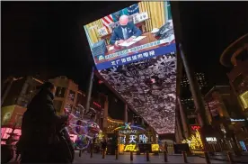  ?? (AP/Mark Schiefelbe­in) ?? A vendor selling lighted balloons stands Thursday near a large video showing a government news report about the inaugurati­on of President Joe Biden at a shopping mall in Beijing.