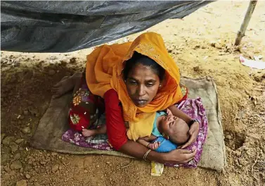  ??  ?? In dire straits: A refugee holding her child as she sits in a makeshift shelter after arriving at the Kutupalong refugee camp near the Bangladesh­i town of Teknaf. — AFP