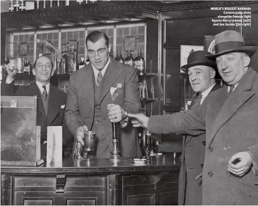  ?? Photo: LARRY BRAYSHER ?? WORLD’S BIGGEST BARMAN: Carnera pulls pints alongside famous fight figures Harry Levene [left] and Joe Jacobs [far right]