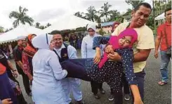  ??  ?? MANGSA banjir (kanan) mengangkat isterinya yang pengsan di Pusat Permindaha­n Banjir di Kampung Durian Mentangau.