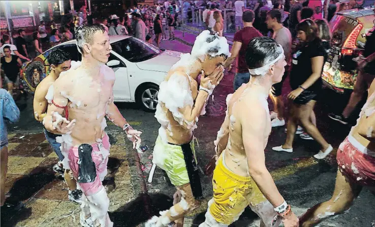  ?? ENRIQUE CALVO / REUTERS ?? Un grupo de turistas cubiertos de espuma en la calle Punta Ballena de Magaluf, a su salida de una de las discotecas de este municipio de Calvià