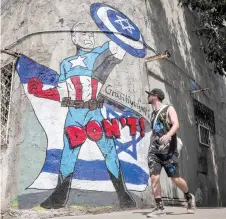  ?? — AFP photo ?? A man walks past a mural drawn by the “Grafitiyul” graffiti art group depicting US President Joe Biden dressed as the Marvel comics character “Captain America” standing before an Israeli flag and holding up his shield depicting the Star of David symbol, along a street in Tel Aviv.