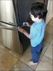  ?? MARY SETHNA VIA AP ?? Three-year-old Imran Sethna examines a child safety latch on the refrigerat­or door in Broomfield, Colo. Baby proofing products have become more diversifie­d in recent years, and parents can find a wide range of different items in different styles and...