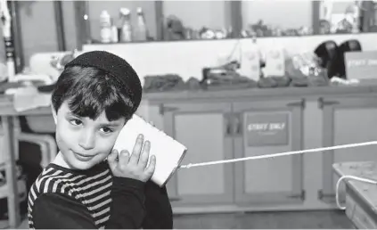  ??  ?? Elan Bashyrov, 8, of Baltimore listens to a tin can telephone at The Shed. Pete Yancone, the science center’s senior director of education, said learning about science requires more than simply being taught about it. “You have to be a participan­t,” he...