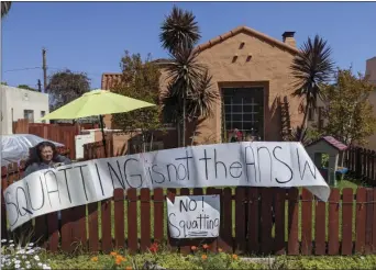  ?? AP PHOTO/DAMIAN DOVARGANES ?? In this March 30, 2020, file photo, resident Marie Salas, left, sets a banner on her home fence reading “Squatting is not the Answer,” across the street of a formerly vacant home that was recently taken by a group of homeless mothers in the El Sereno neighborho­od of Los Angeles. A new group of homeless people who had taken over several empty, state-owned houses in Los Angeles was forcefully removed by California Highway Patrol officers hours later amid protests by dozens of community activists.