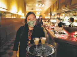  ??  ?? Manager Samantha McGrath holds cappuccino­s for guests seated outside at Tosca Cafe, where dinner service has resumed after a closure.