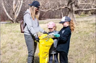  ?? HERALD PHOTO BY JUSTIN SEWARD ?? Keely Kavanagh helps Eliza and Eesia Semenuik fill their bag full of garbage Friday during the Coulee Clean-up in the city’s river valley.