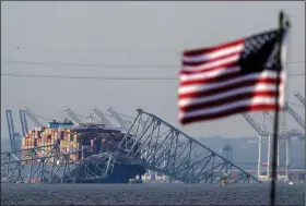  ?? (File Photo/AP/Mark Schiefelbe­in) ?? A U.S. flag flies on a moored boat Tuesday as the container ship Dali rests against the wreckage of the Francis Scott Key Bridge as seen from Pasadena, Md.