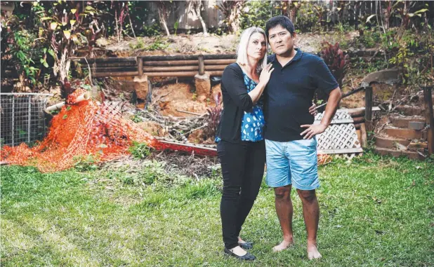  ?? Picture: BRENDAN RADKE ?? SHOCKED: Redlynch Valley residents Noriaki and Jodie Hogan experience­d severe damage to their backyard retaining wall during flooding in March. Despite having documents stating flooding and retaining walls are covered, their insurance claim has been rejected.