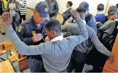  ?? PICTURE: TRACEY ADAMS ?? RAID: Police officers search pupils at Fezeka High School in Gugulethu, during which they said they confiscate­d two knives. Two pupils were then escorted to a police van and placed inside.