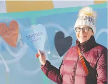  ??  ?? Bridgeland resident Christine Rogerson and other community members were covering up graffiti with paper hearts on Monday as businesses in the community where tagged with spray paint over the weekend.