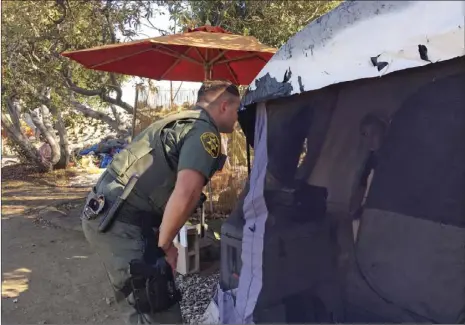  ?? AP PHOTO/AMY TAXIN ?? An Orange County sheriff’s deputy calls to residents inside a tent in Anaheim on Monday to let them know they’ll need to leave the area and that the county will assist with the move if they need. Southern California authoritie­s Monday went tent to tent...