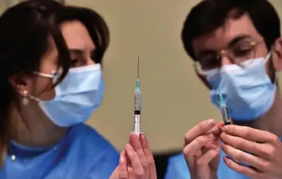  ?? GETTY IMaGES PhOTOS ?? WAYS TO GO: Health workers prepare syringes with doses of the Pfizer vaccine in Toulouse, southern France, on Saturday. A Johns Hopkins expert says the U.S. won’t achieve herd immunity until children are vaccinated, but the country will need more supply, below, to reach that goal.