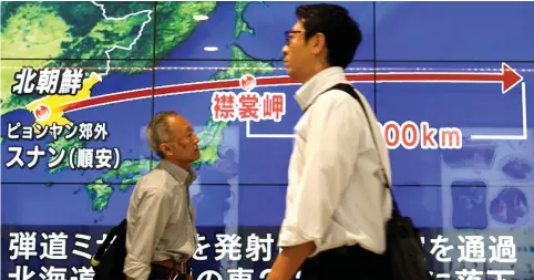  ??  ?? PEDESTRIAN­S WALK past a street monitor last month in Tokyo showing a news report about North Korea’s nuclear test.