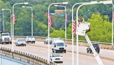  ?? STAFF PHOTO BY ERIN O. SMITH ?? Eddie Poe, a traffic technician with the Chattanoog­a Department of Transporta­tion, installs an American flag over Veterans Bridge on Monday. A flag raising ceremony was held nearby, at the Bluff View Art District Sculpture Garden.