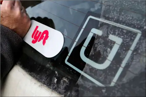  ?? AP FILE PHOTO/GENE J. PUSKAR ?? In this 2018 file photo, a Lyft logo is installed on a Lyft driver’s car next to an Uber sticker in Pittsburgh.