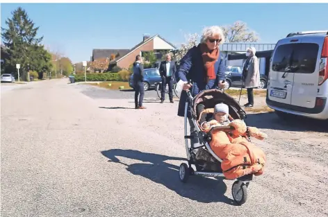  ?? RP-FOTO: KLAUS NIKOLEI ?? Weil es an der Straße Am Friedensho­f in Obrighoven keinen Fußweg gibt, muss Sabine Richenhage­n den Kinderwage­n, in dem Enkel Paul (13 Monate) sitzt, über die Straße schieben. Dahinter diskutiere­n Anwohner mit der Verwaltung über eine Lösung des Problems.