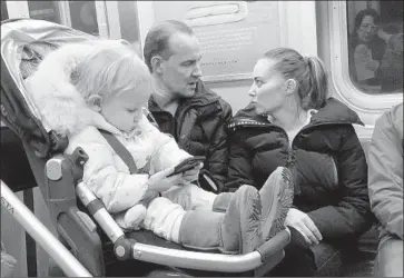  ?? Mark Lennihan Associated Press ?? A YOUNG GIRL plays with a mobile phone while riding in a New York subway. Two major Apple investors have urged the iPhone maker to create ways for parents to restrict children’s access to their mobile phones.