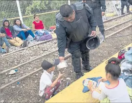  ?? MOISES CASTILLO — THE ASSOCIATED PRESS ?? A Guatemalan police officer gives a migrant child some food as the migrants, bound for the U.S.-Mexico border, wait on a bridge that stretches over the Suchiate River, connecting Guatemala and Mexico, in Tecun Uman, Guatemala, early Saturday.