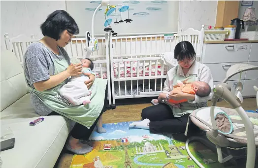  ??  ?? ROCKING THE CRIB: Social workers at the Jusarang Community Church in Seoul. The number of abandoned babies in South Korea has jumped.