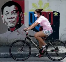 ?? AP ?? A woman wearing a protective mask rides her bicycle past an image of Philippine President Rodrigo Duterte in Manila. The Philippine­s is indefinite­ly banning the entry of foreigners after the government declared a state of calamity and public health emergency amid the coronaviru­s outbreak.
