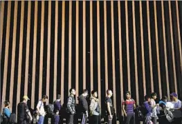  ?? Gregory Bull Associated Press ?? MIGRANTS line up against a border wall as they wait to apply for asylum after crossing the border from Mexico in July near Yuma, Ariz.