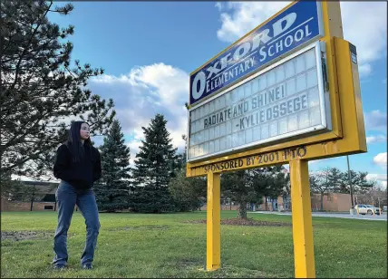  ?? ?? Kylie Ossege stands outside Oxford Elementary School on Nov. 11, 2021, in Oxford Township, Mich. The sign outside the school features a phrase — “radiate and shine” — that Ossege used as part of her commenceme­nt address at Oxford High School in 2022.