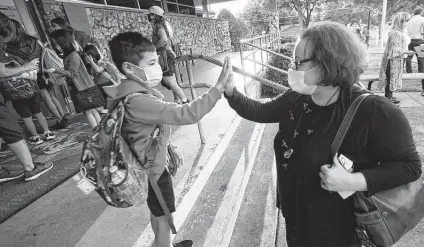  ?? LM Otero / Associated Press ?? Maksim Mongayt, 7, gives his mother, Alexandra, a high-five before his first day of classes in Richardson on Tuesday. Despite Gov. Greg Abbott’s order banning mask mandates, 58 school districts across the state are requiring masks for students.