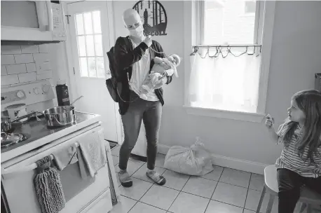  ?? ROBERTSON/PHILADELPH­IA INQUIRER/ TNS] ?? Lisa Oney juggles her chemothera­py treatment bag on her right shoulder and 3-month-old Jack O'Driscoll in her left arm while daughter Fiona O'Driscoll, 3, has a snack in the kitchen. Lisa was getting her chemothera­py treatment at her Souderton, Pa., home on Jan. 16. [ELIZABETH